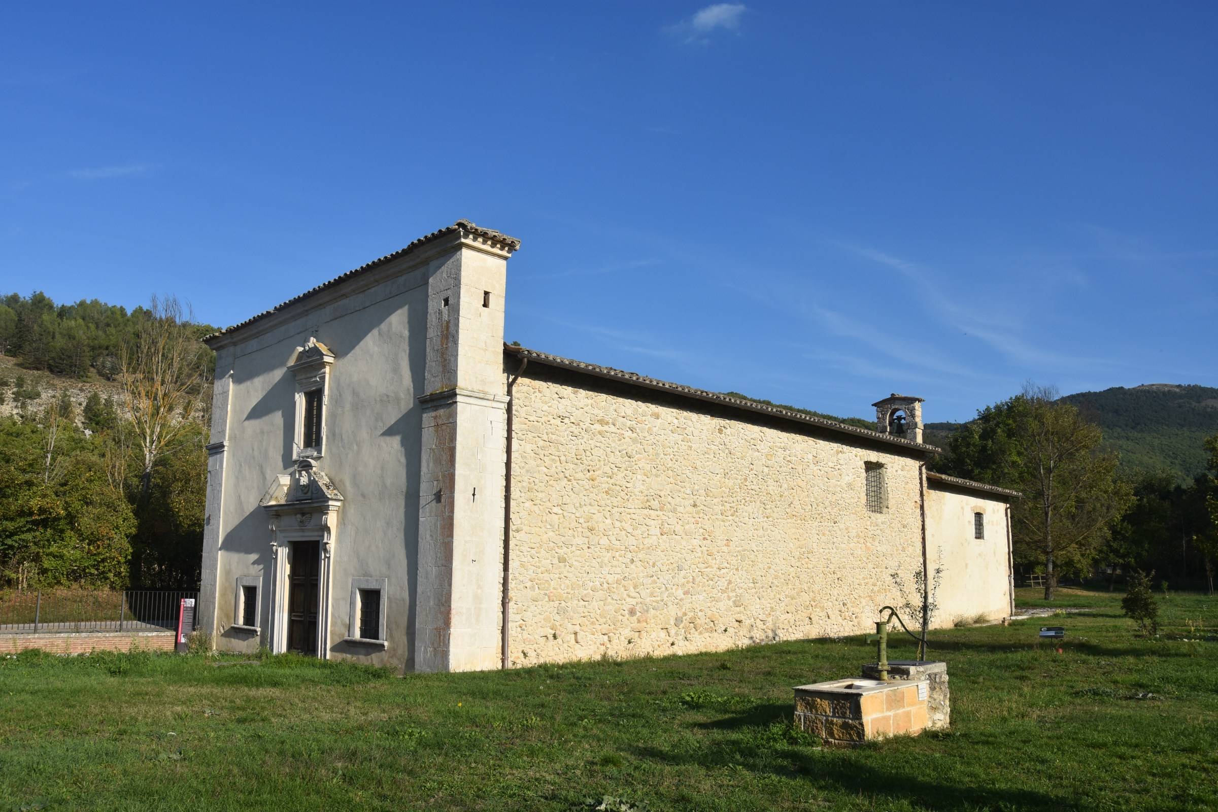 foto laterale della chiesa con il piccolo campanile e la fonta di acqua non potabile